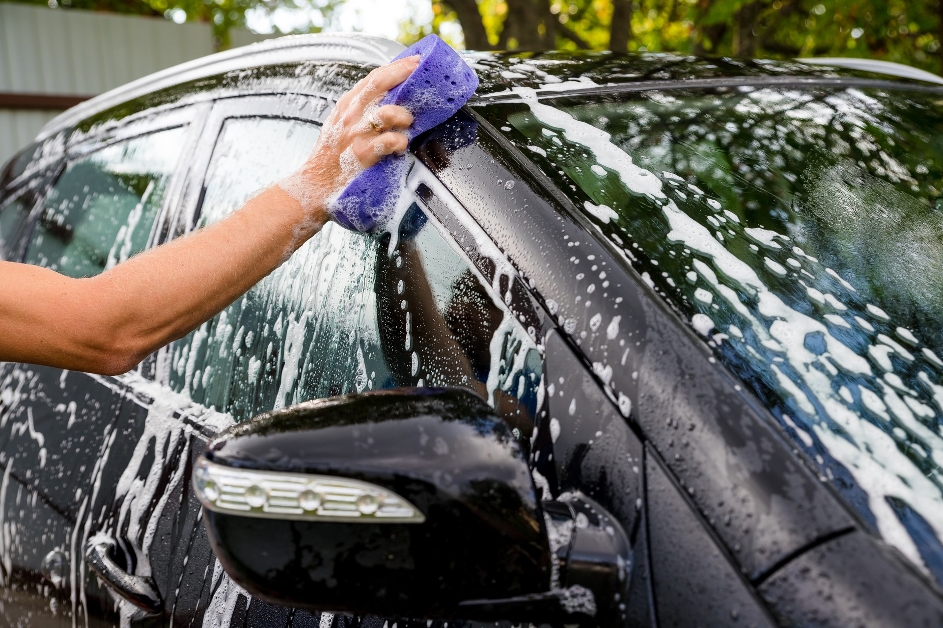 woman washing automobile at manual car washing self service station, cleaning with foam, pressured water. Transportation, auto, vehicle care concept